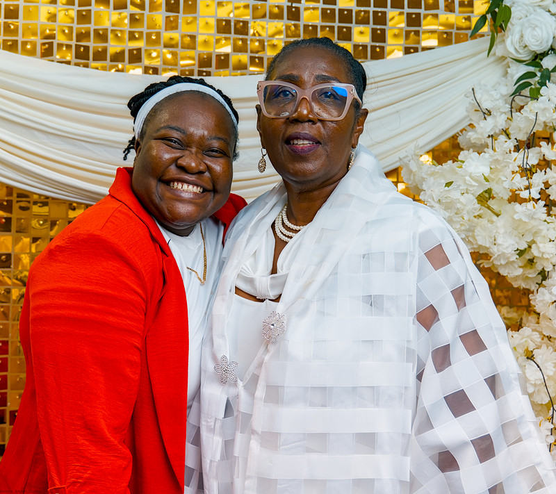 Two women in white and red share a wide smile at the photo wall