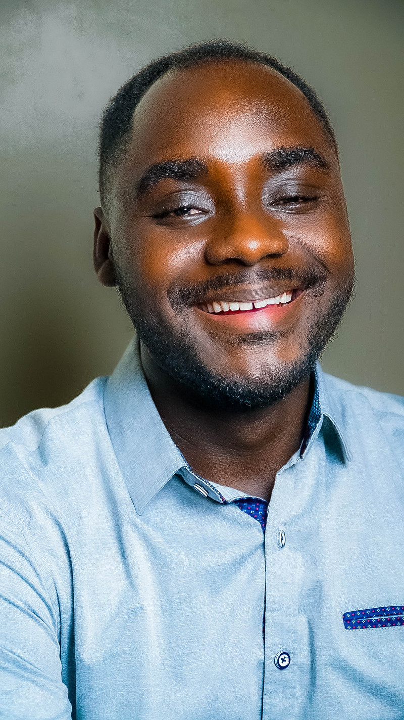 Portrait of Prince Adufah, founder of Kwame Adufah Studios, smiling in a light blue shirt