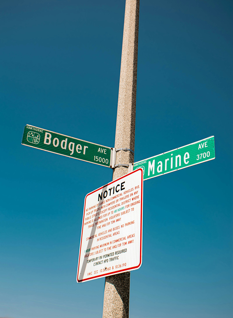 Street name signs on a concrete pole against a teal sky